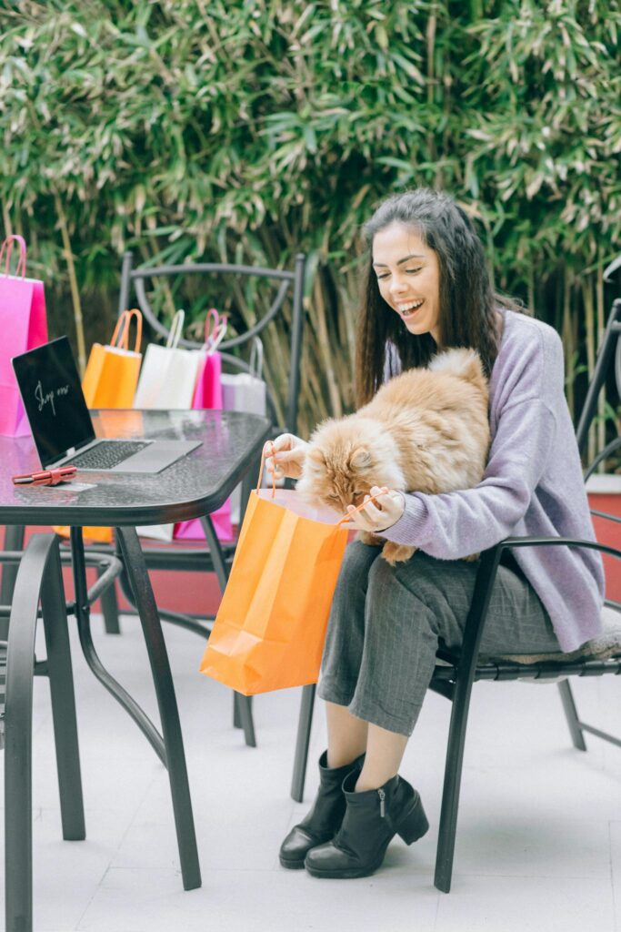 Woman in Purple Long Sleeve Shirt Sitting on Black Chair Beside Orange Tabby Cat